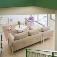 Beige couch with light wood legs, colorful patterned area rug, green walls, and purple accent chair. Modern decor style.