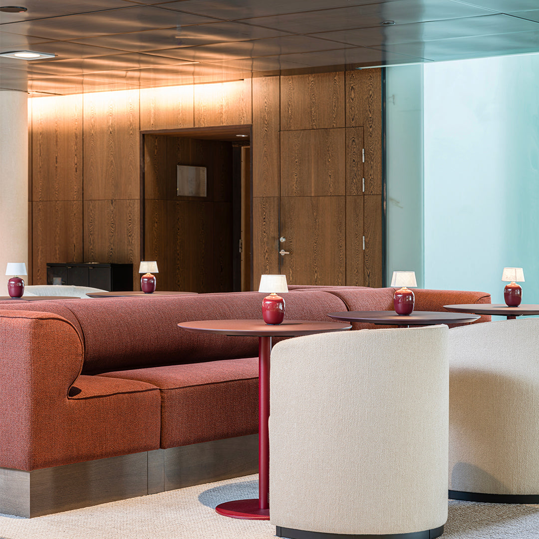 Rust-colored upholstered sofa and cream circular chairs with red accent tables in a modern lounge setting.