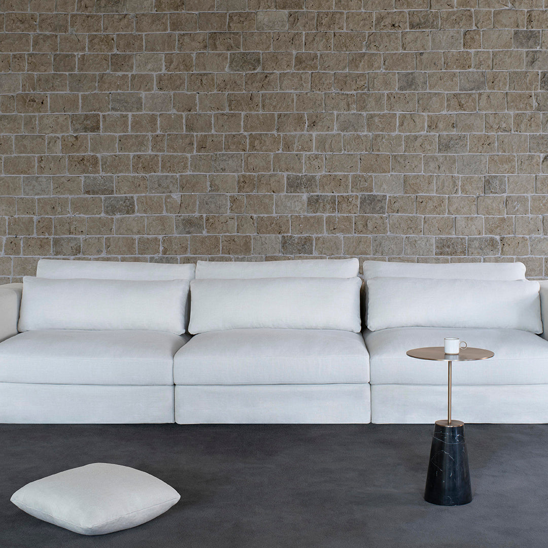 Modern white couch on a textured stone wall backdrop, featuring clean lines and minimalistic design.