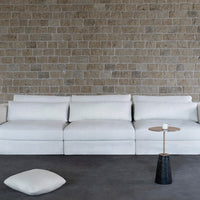 Modern white couch on a textured stone wall backdrop, featuring clean lines and minimalistic design.