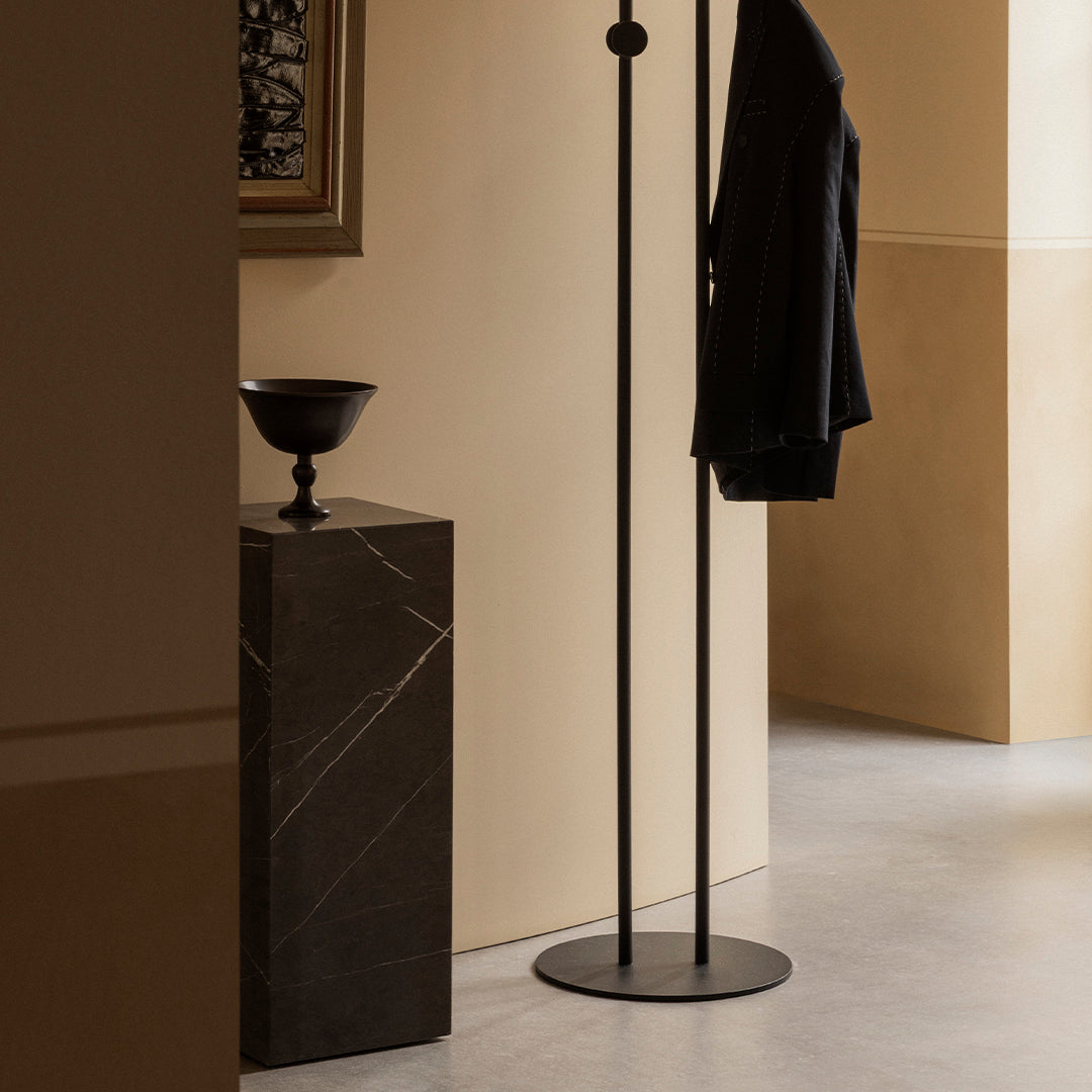 Minimalist black coat rack against a warm beige wall, complemented by a dark marble pedestal and stylish decor.