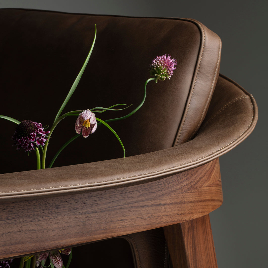 Brown leather chair with floral embellishments, featuring soft curves and natural wood accents. Elegant and modern design.
