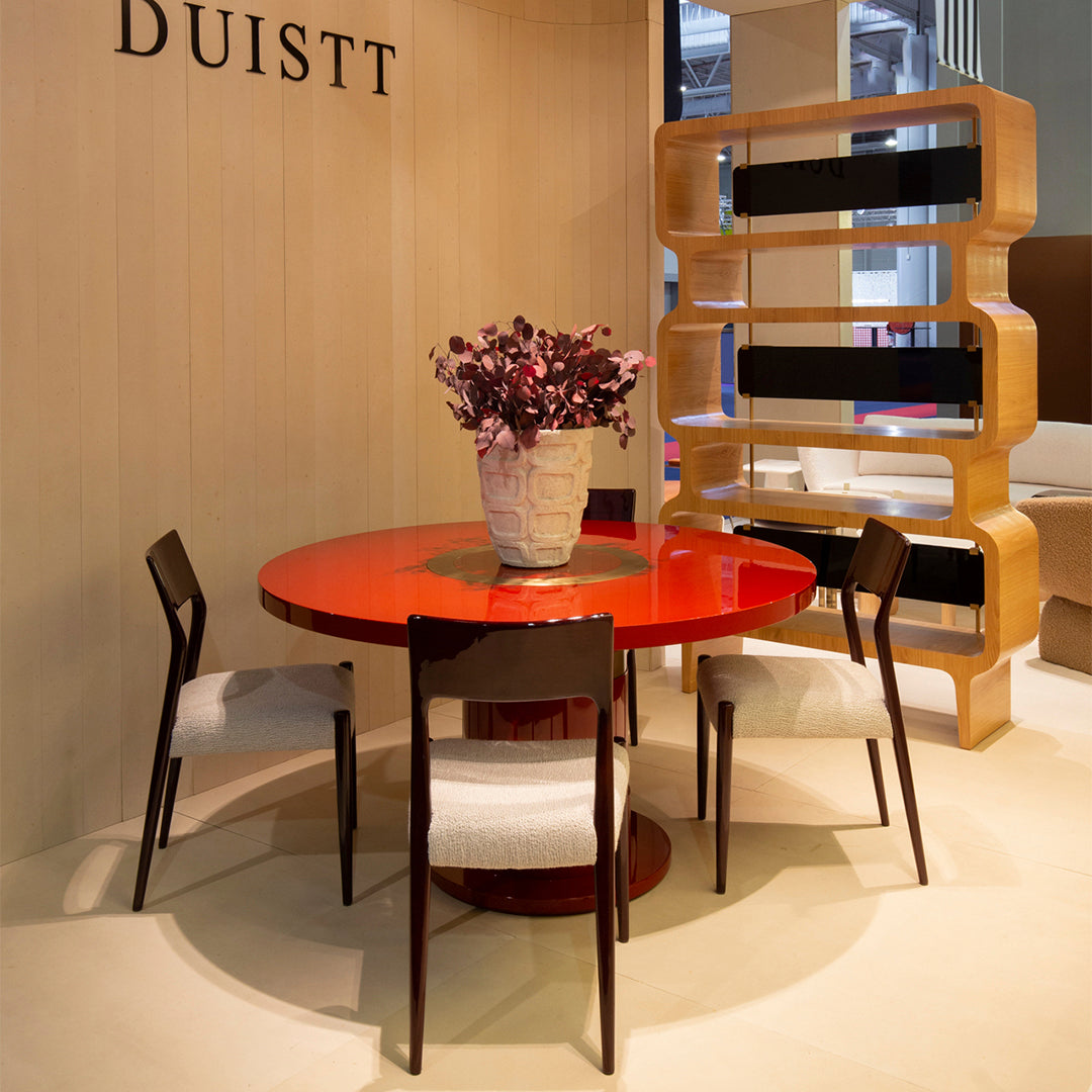 "Vibrant red circular dining table with four black chairs and a textured beige wall background."