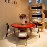 "Vibrant red circular dining table with four black chairs and a textured beige wall background."
