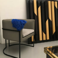 Modern gray chair with a blue faux fur throw, set against a geometric black and gold patterned backdrop.