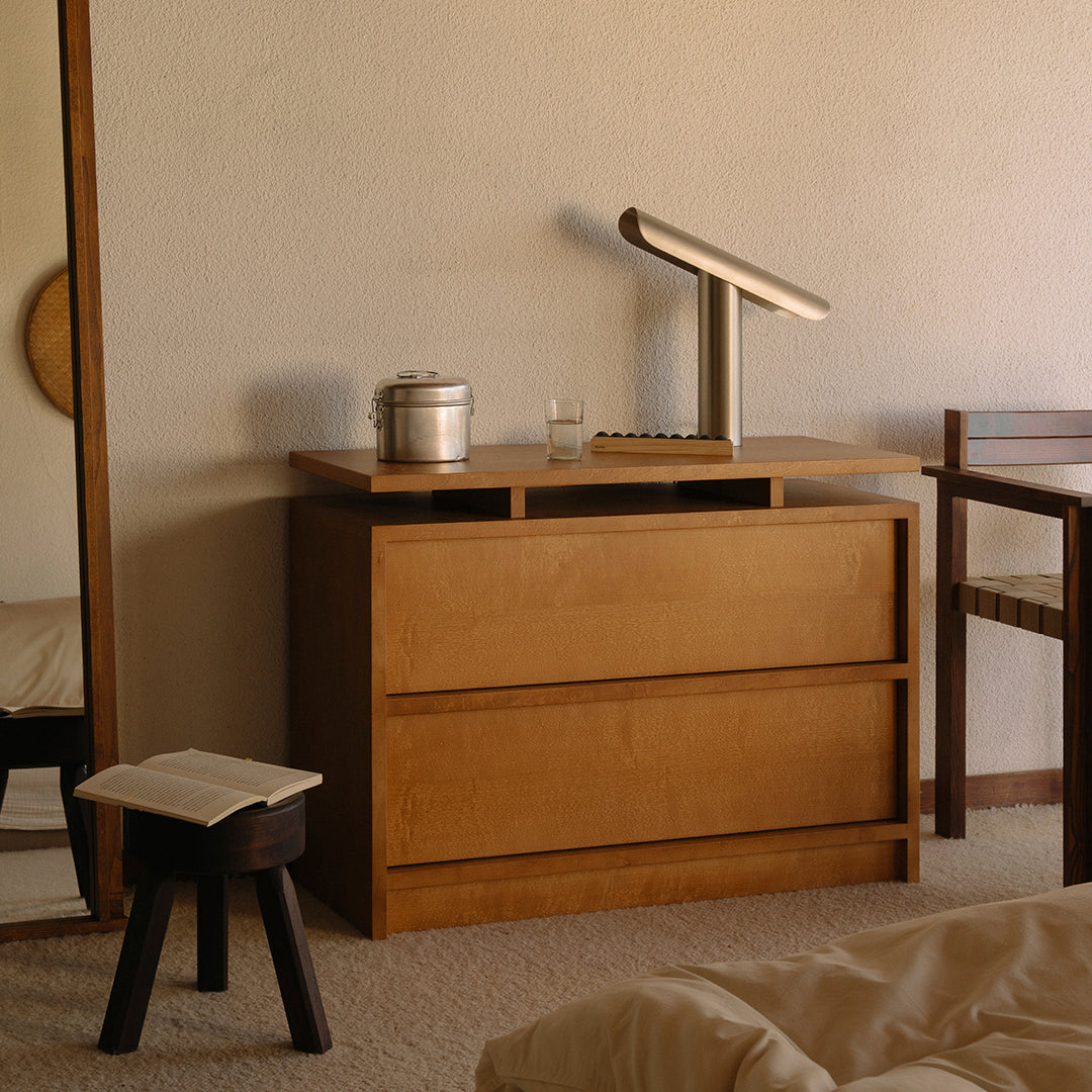 Natural wood dresser in warm tones, featuring a smooth finish and minimalist design, complemented by a simple table lamp.