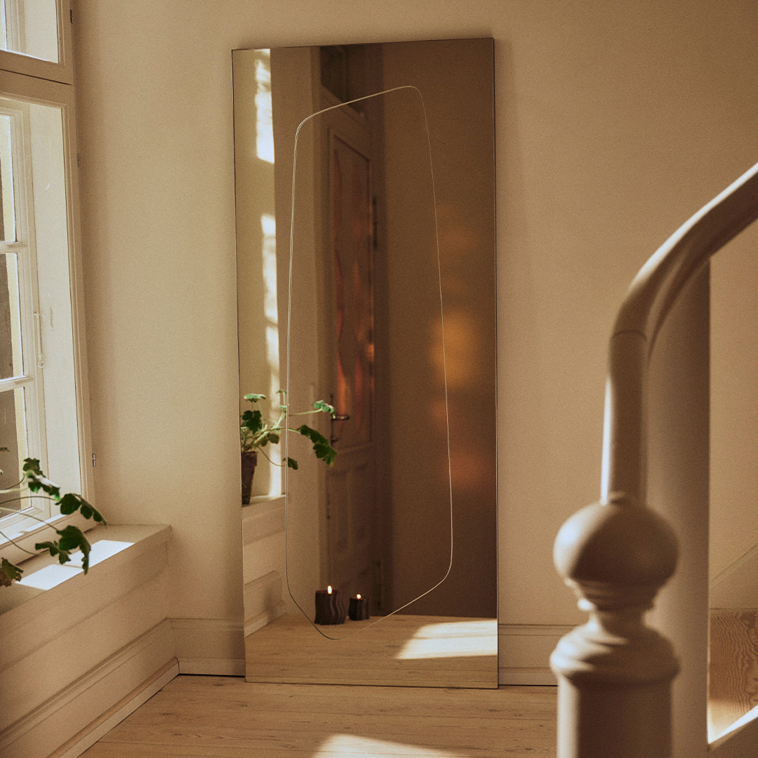 Full-length mirror with a sleek, reflective surface, framed in warm tones, complemented by soft natural light.