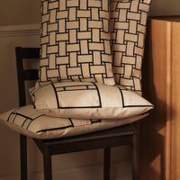 Cream pillows with a black geometric pattern stacked on a wooden chair. Perfect for modern decor.