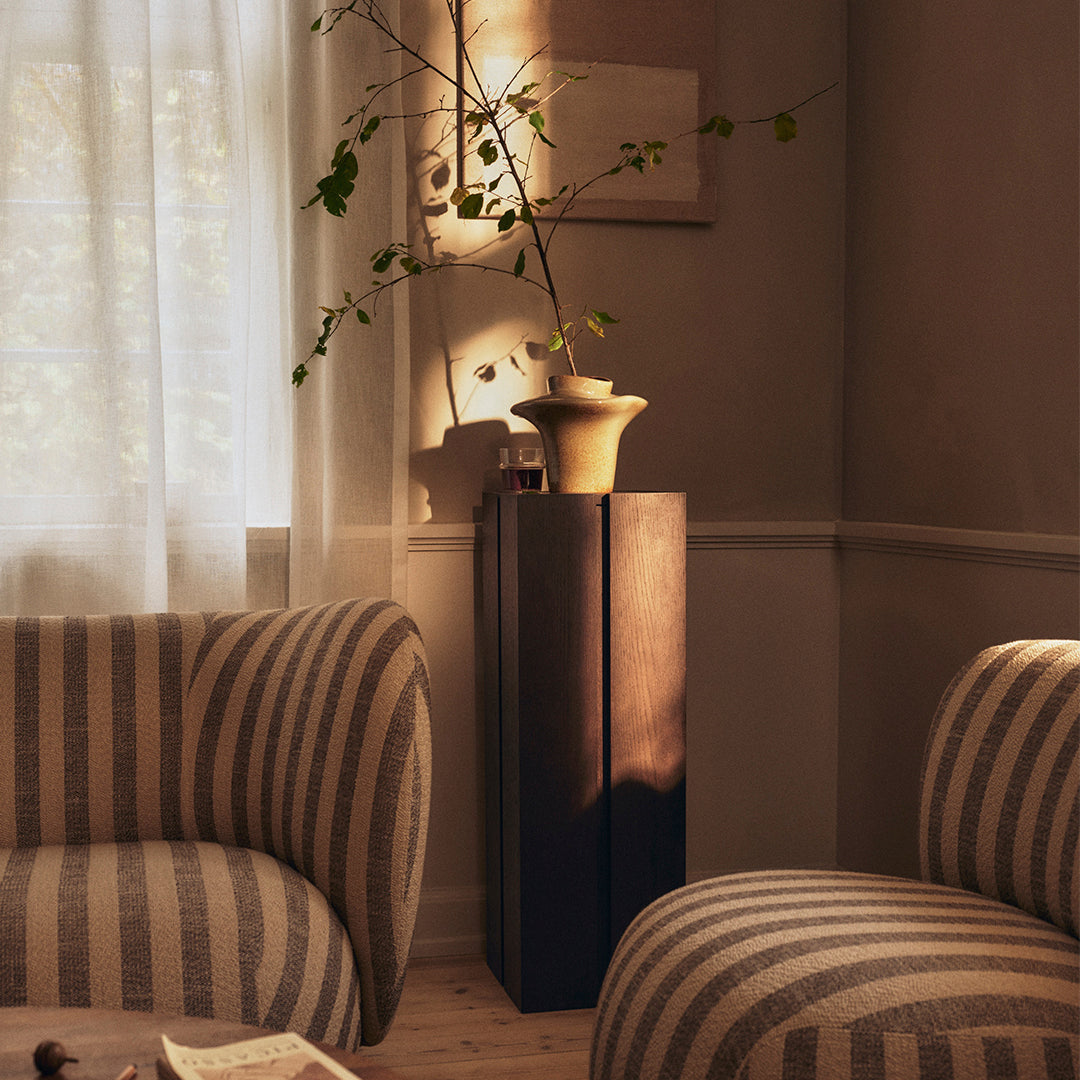 Striped beige and cream upholstery on cozy armchairs contrasts with a sleek, dark wooden pedestal.