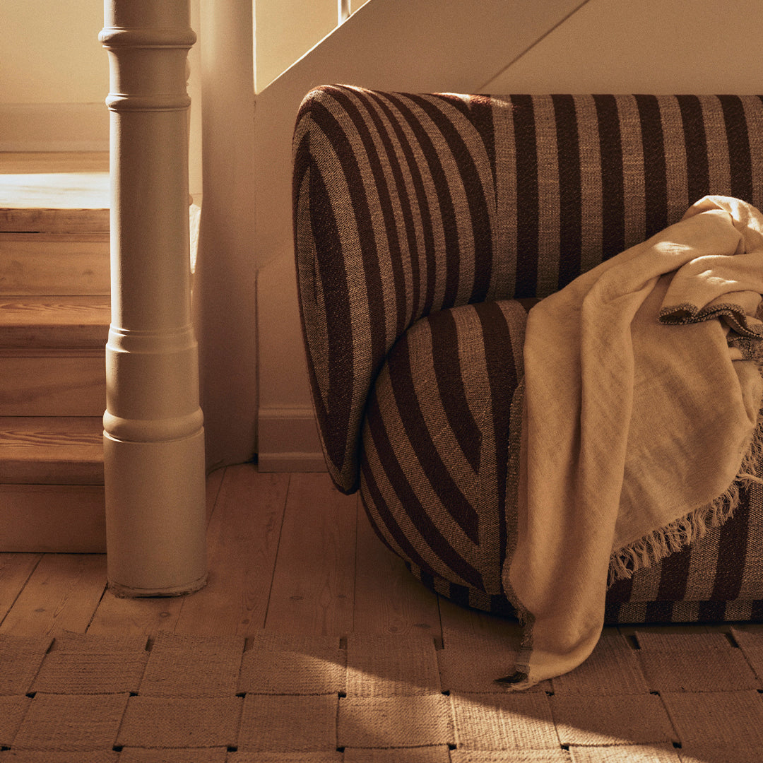 Brown and beige striped couch with a soft neutral throw, set against a warm light and wooden staircase.