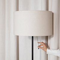 Beige linen lamp shade with black base, featuring a smooth, minimalist design against light curtains.