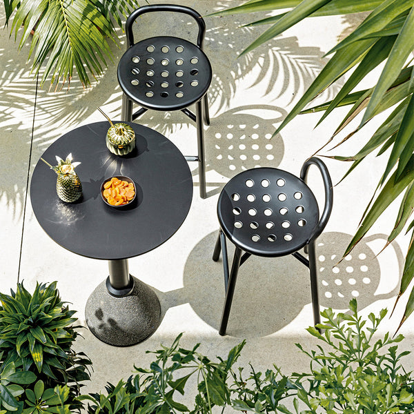 Black round table and dotted chairs surrounded by lush green plants, featuring a modern design and contemporary aesthetic.