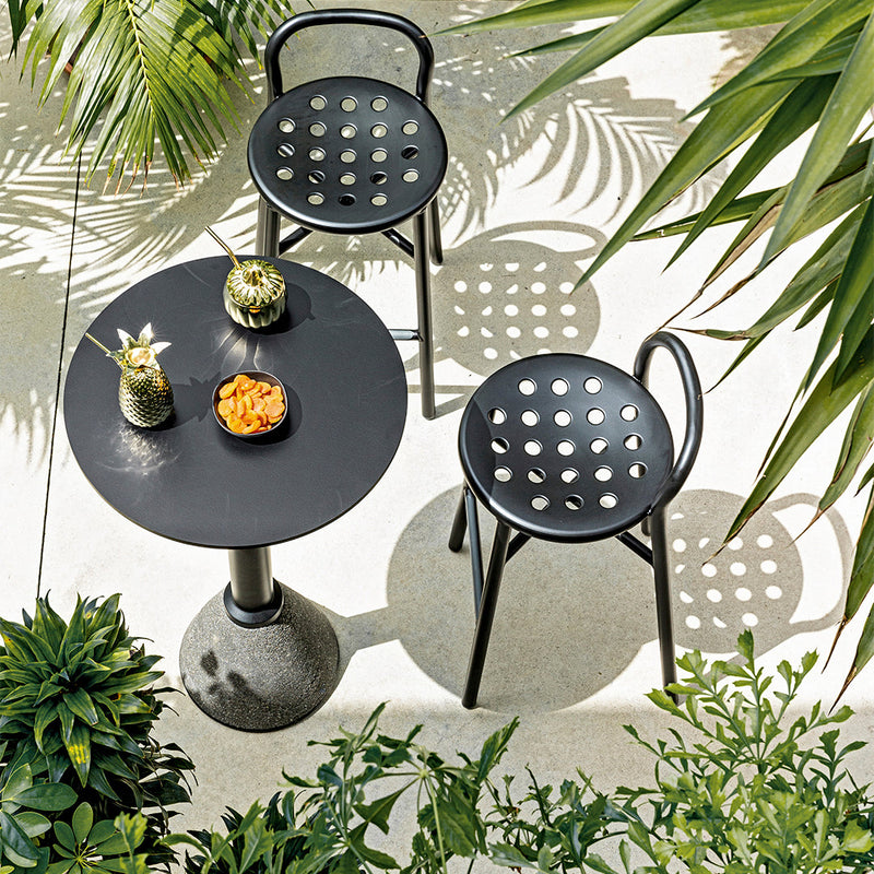 Black round table and dotted chairs surrounded by lush green plants, featuring a modern design and contemporary aesthetic.