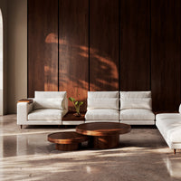 White modern sofa set with soft textures, accented by rich wooden coffee tables against a dark wooden wall.