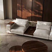 Modern white sectional sofa with textured cushions and rich wooden accents, set against a sleek concrete background.