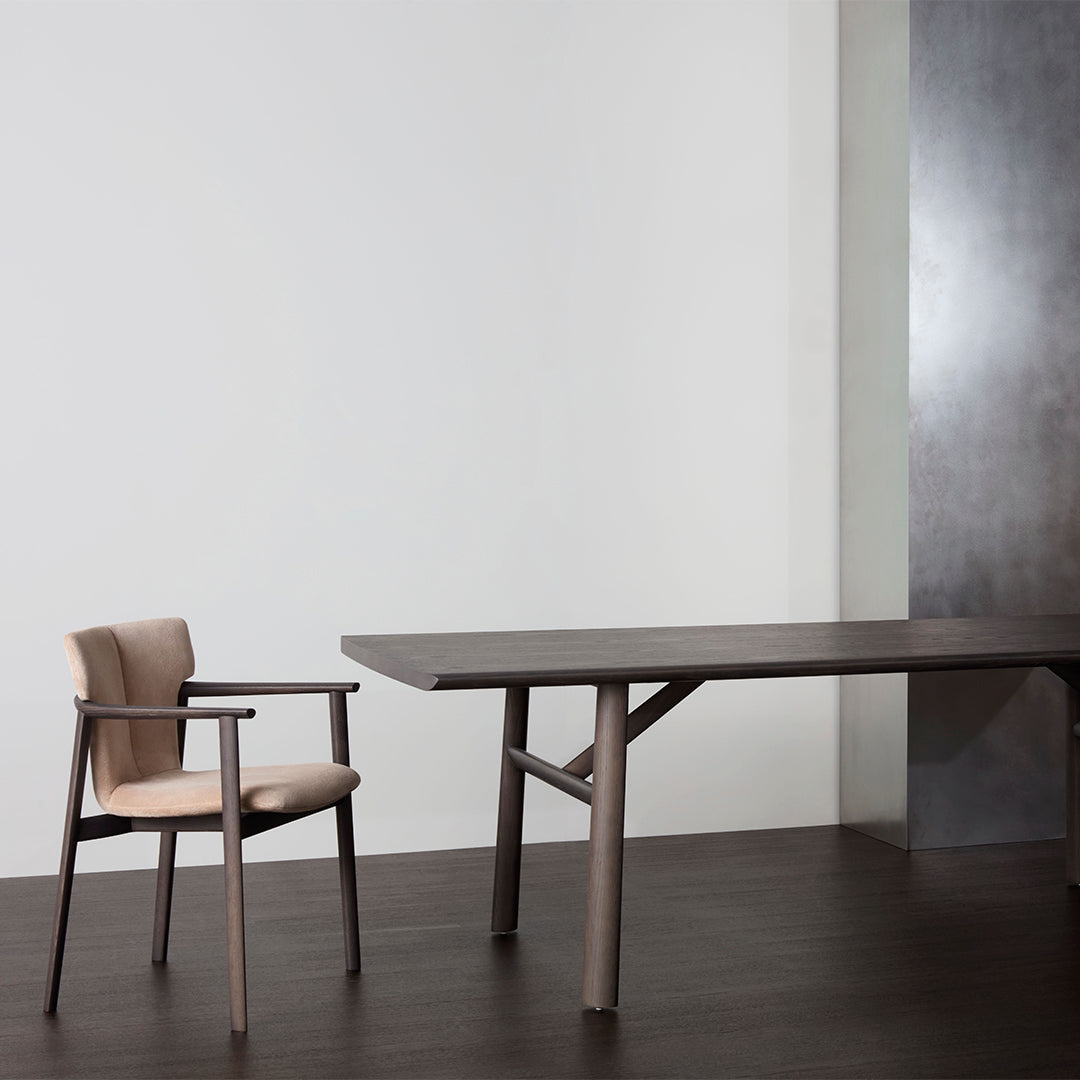 Modern wooden dining table in dark brown with a beige upholstered chair against a neutral background.
