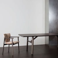 Modern wooden dining table in dark brown with a beige upholstered chair against a neutral background.
