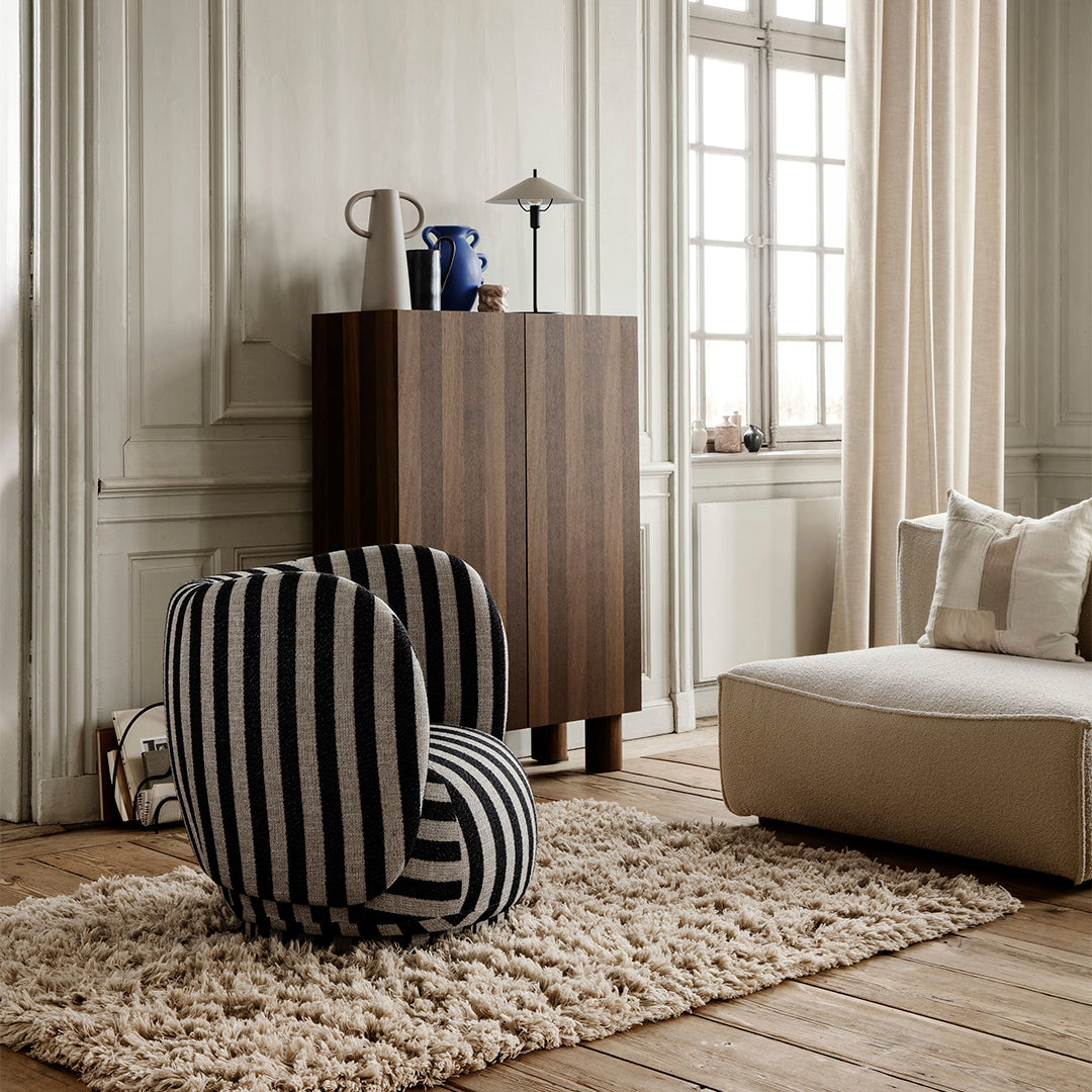 Black and white striped chair on a plush rug, set against a light-toned wood floor and neutral walls.