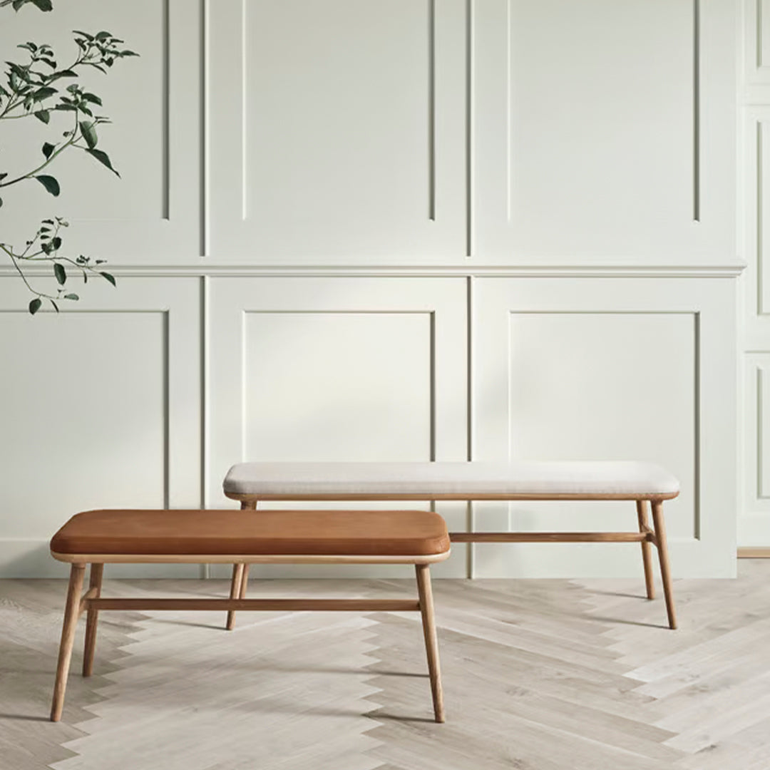 Two minimalist benches, one in warm wood tones, the other in soft white upholstery, set against a pale green wall.