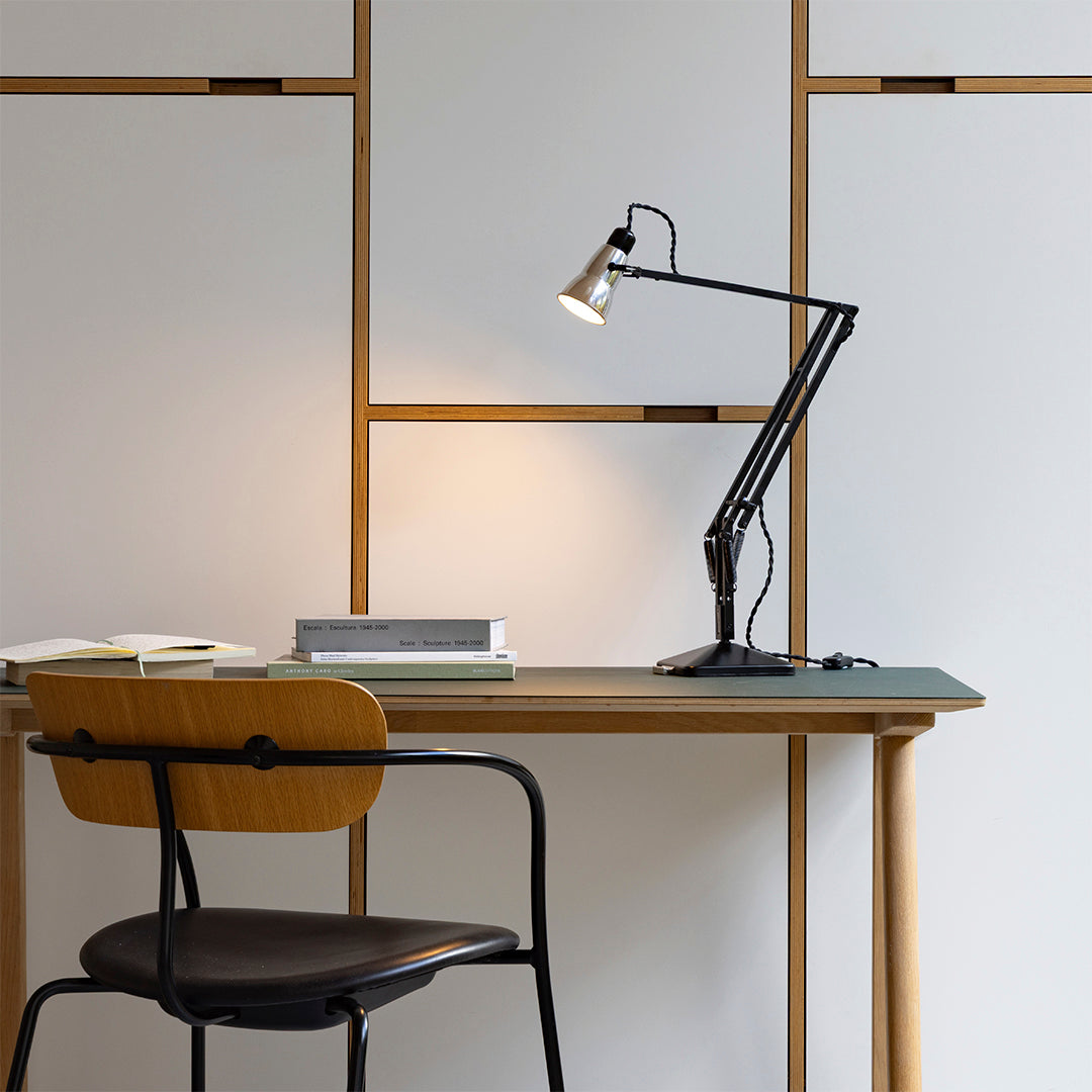 Black desk lamp on a wooden desk with sleek white panels and a minimalist black chair. Clean, modern aesthetics.