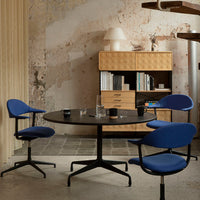 Modern dining area featuring deep blue chairs, a dark round table, and warm beige storage against a textured wall.