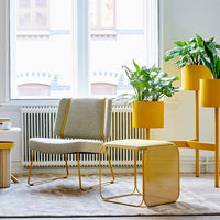 Gray upholstered chair with yellow metal accents, matching yellow planter, and a light textured rug. Bright, modern decor.