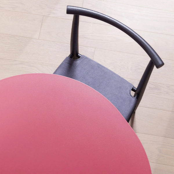 Round pink table with a gray upholstered chair showcasing a subtle dotted pattern and smooth finishes.
