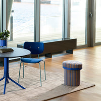 Blue chair with light blue legs next to a patterned stool featuring navy, white, and red tones in a modern interior.