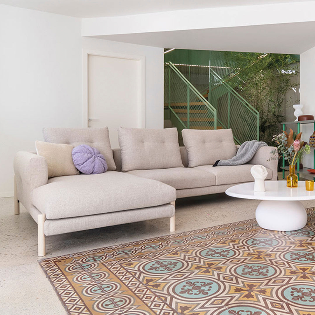 Neutral beige sectional sofa with pastel purple pillow, paired with a colorful patterned area rug featuring intricate designs.