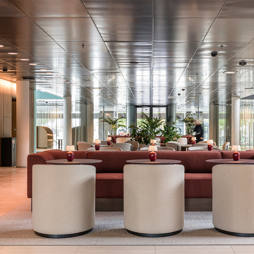 Stylish red sofa and cream cylindrical tables against a sleek, mirrored backdrop in an elegant lounge setting.