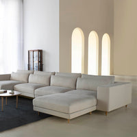 Light beige sectional sofa with smooth fabric and subtle design, complemented by a dark area rug and minimalist decor.
