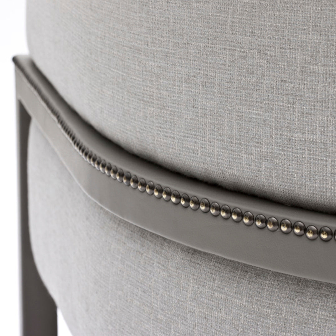 Grey upholstered chair featuring a textured fabric and decorative silver nailhead trim. Elegant and modern design.