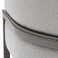 Grey upholstered chair featuring a textured fabric and decorative silver nailhead trim. Elegant and modern design.