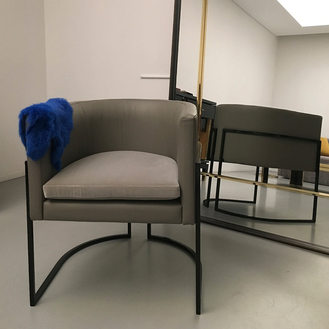Gray upholstered chair with a sleek black frame, accented by a vibrant blue throw blanket. Modern design and minimalist style.