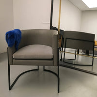 Gray upholstered chair with a sleek black frame, accented by a vibrant blue throw blanket. Modern design and minimalist style.