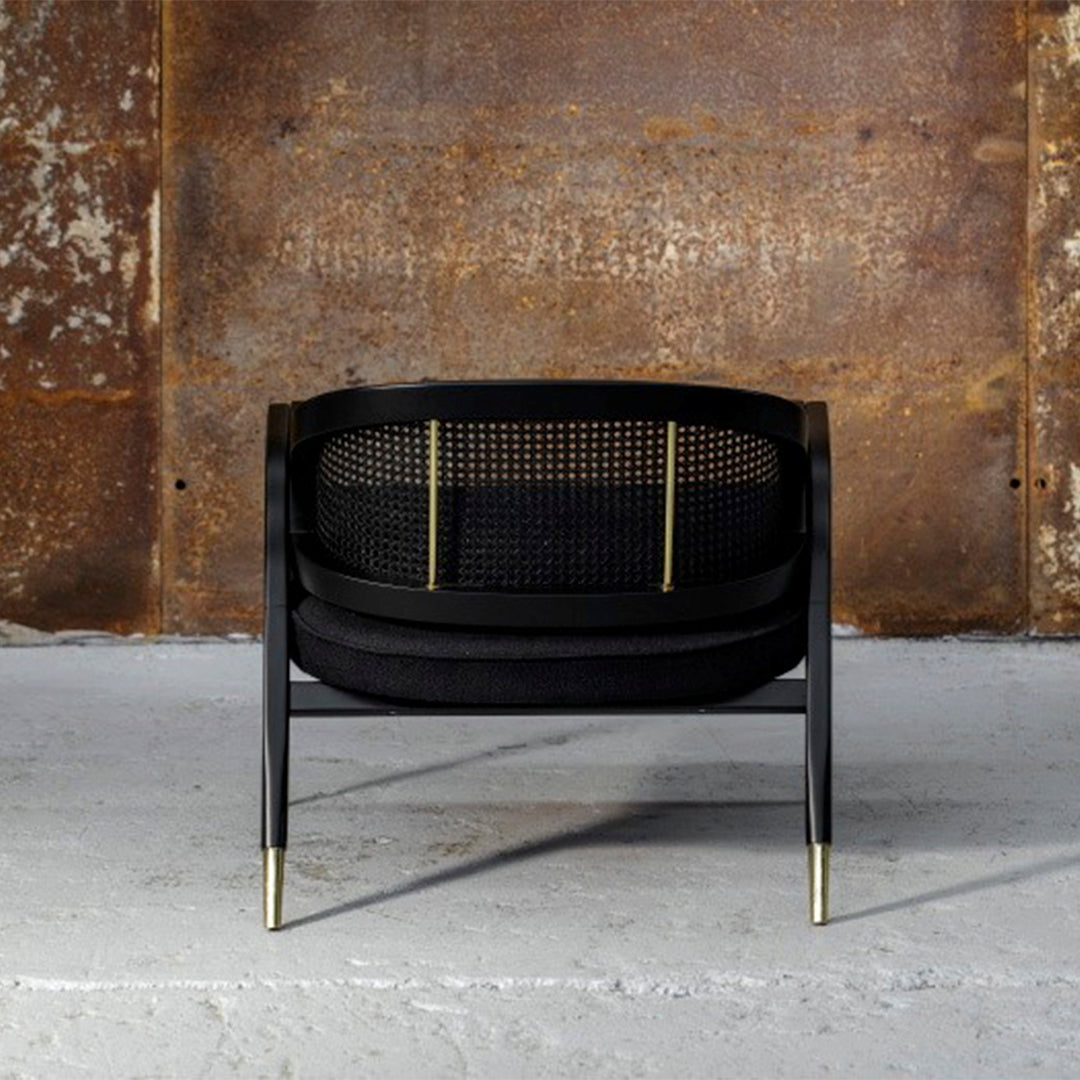 Black woven chair with a textured mesh back and gold accents, set against a rustic, weathered metal backdrop.