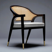 Black wooden chair with caned back, light gray cushion, and gold-tipped legs, featuring a modern design.