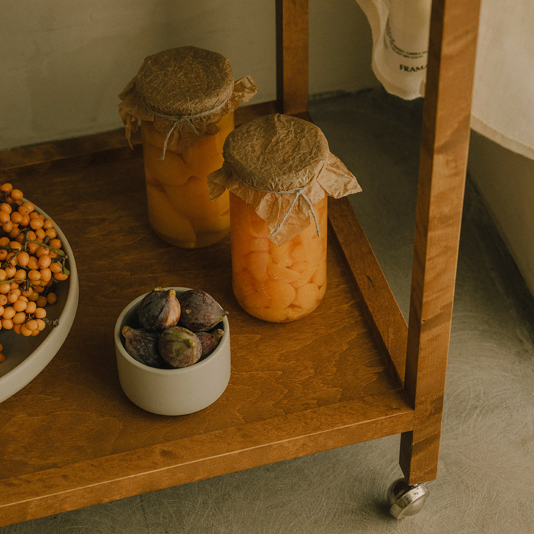 "Two amber jars with burlap lids and a small white bowl of colorful fruits on a wooden shelf."