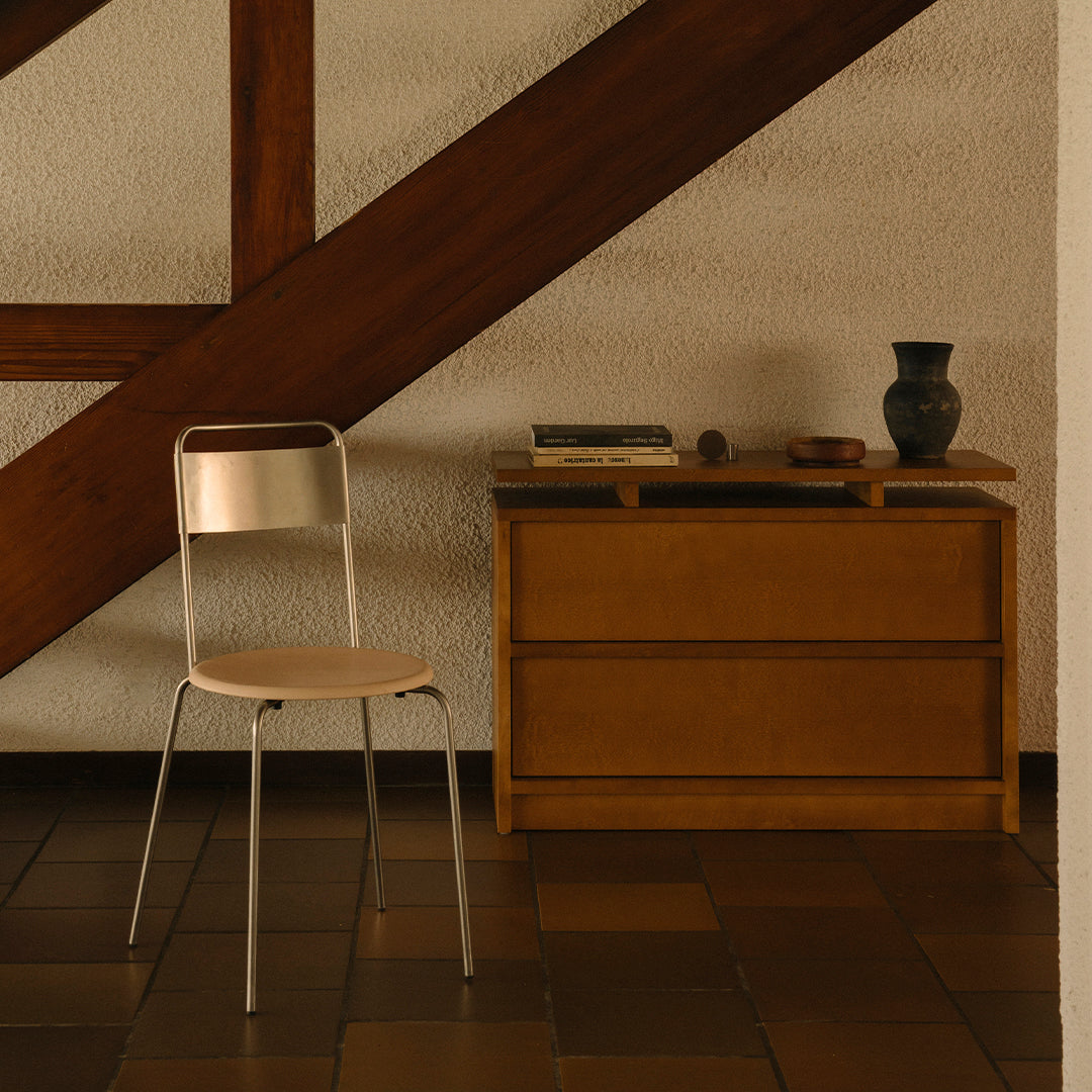 "Minimalist chair with a natural wood seat and silver metal frame, set against a warm brown and beige backdrop."