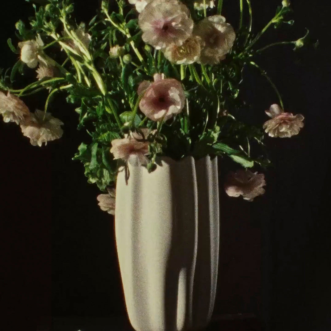 "Soft pink flowers in a textured cream vase against a dark background, showcasing delicate hues and organic shapes."