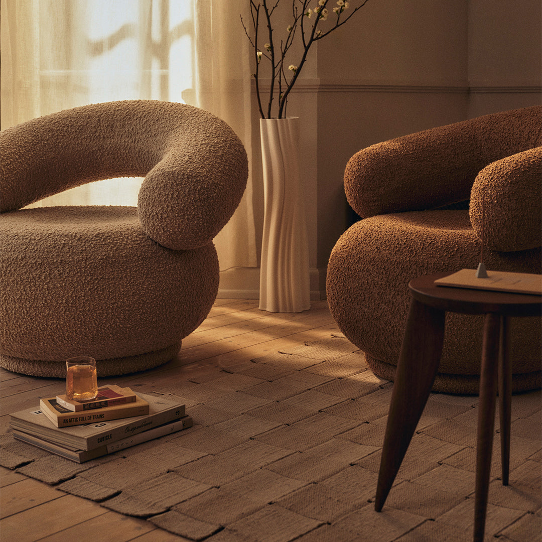 Two plush, curved armchairs in warm beige and soft brown with textured fabrics, set in a cozy, minimalist atmosphere.