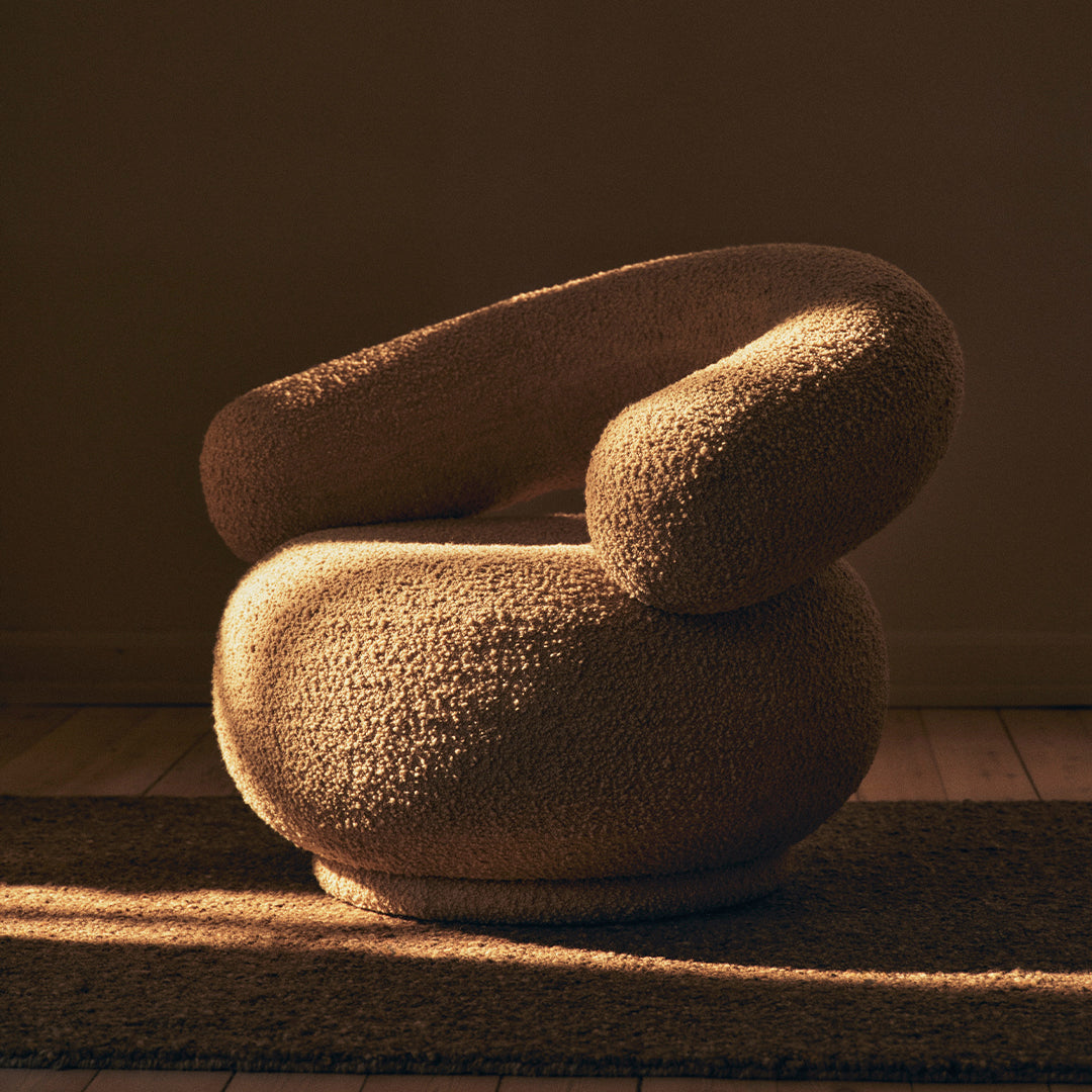 Cozy beige armchair with a rounded shape and textured surface, featuring soft curves and warm tones. Perfect for modern decor.