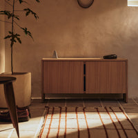 Natural wood cabinet with warm tones, paired with a textured cream and rust-striped rug on a tiled floor.