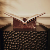 "Open book with glossy white pages on a rich red marble base, set against a textured black wood background."