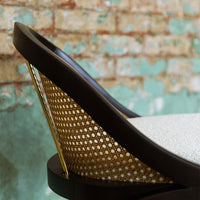 Brown and gold chair with a unique perforated design against a textured green and brick background.