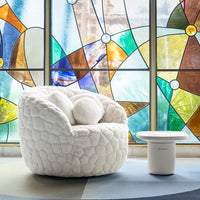 Cozy white textured chair with circular cushions against vibrant stained glass backdrop featuring colorful geometric patterns.