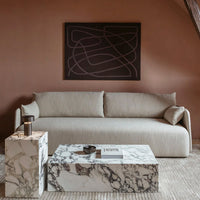 Neutral beige sofa with soft lines beside marble coffee tables featuring bold gray and white veining against a warm backdrop.