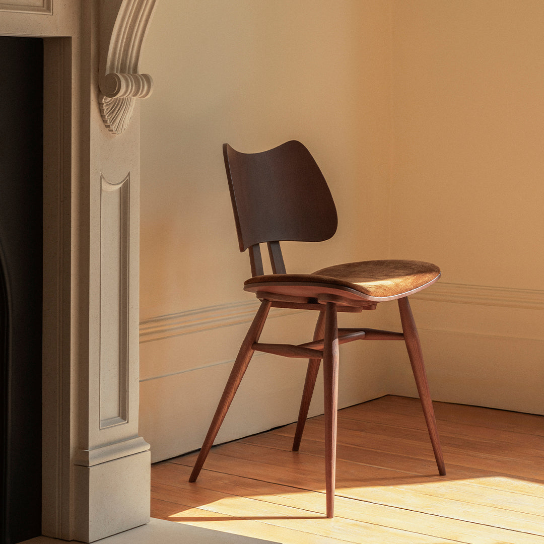 Mid-century wooden chair in rich brown tones with a minimalist design, set against a warm, sunlit interior.