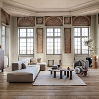 Modern living room featuring a neutral sofa, striped armchair, and earthy tones in decor and flooring. Bright, airy ambiance.