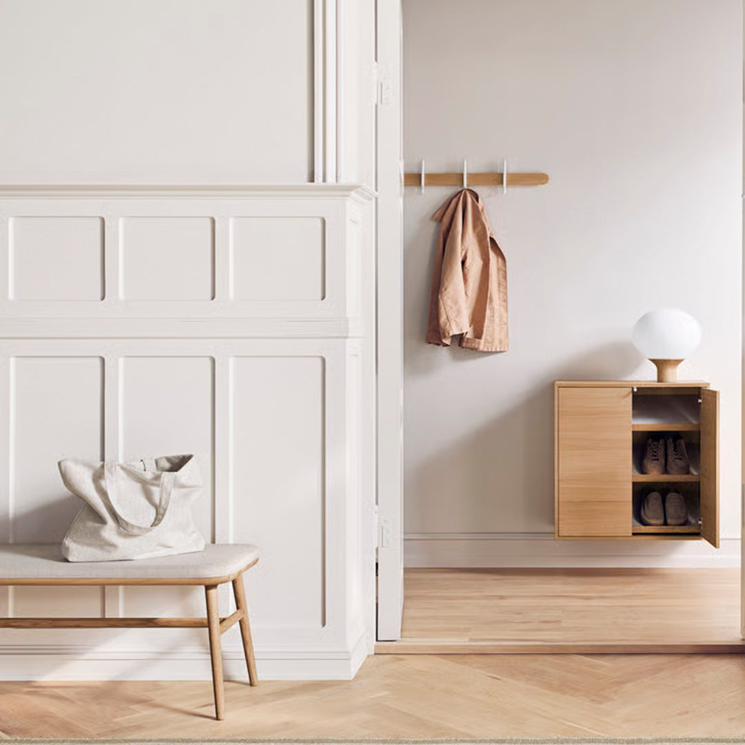 Light wood bench and cabinet against a soft beige and white wall, with a neutral-toned coat and bag for a modern, minimalist look.
